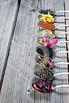 Various kinds of tea in spoons on wooden background. Dry Tea assortment.