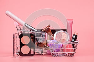 Various make-up products and brushes in shopping cart on pink background. Makeup cosmetics sale concept