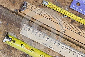 Various measuring sticks, rulers, tape measures on scratched workshop table