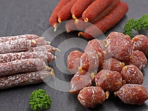 various meat snacks composition, close up of serveral air dried mini salamis on black slate plate
