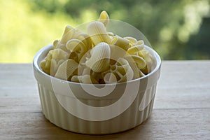 Various mix of pasta in white baking bowl on wooden table, dry ingredients