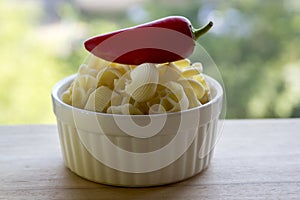 Various mix of pasta in white baking bowl on wooden table and ripened red jalapeno pepper