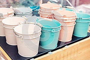 Various multicolored bright small ornamental metal buckets for sale on wooden table outdoors. Many colorful decorative mini pails