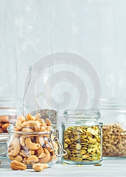 Various nuts and seeds in glass jars over white wooden table against white background