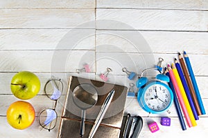 Various office stationery, notepad, clock, pencils, ooh, glasses, pen and two fresh apples on a white wooden table. Top view with