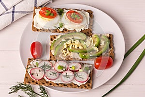 Various open sandwiches with cheese, avocado, radish and egg on a white plate, top view