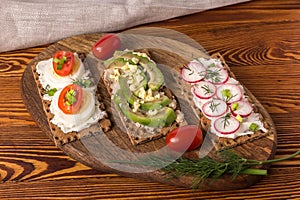 Various open sandwiches with cheese, avocado, radish and egg on a wooden cutting board, horizontal orientation.