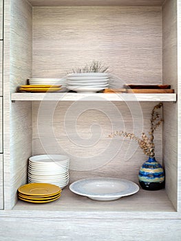 Various orderly white and yellow ceramic dishes in wooden cupboard