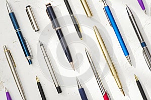 Various pens with and without caps on textured light background