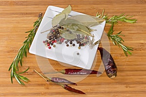 Various peppercorns, dried spices on square saucer, chili, fresh rosemary