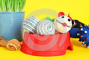 Various pet toys, bowl and wheatgrass on yellow background, closeup