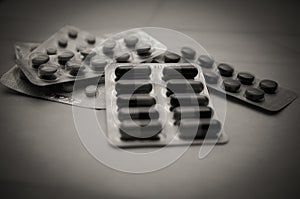 Various pills and capsules in blisters close-up, soft focus . Black and white photo with vignetting. The concept of harm from photo