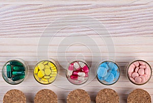 Various pills and capsules on light wooden table top view
