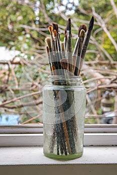 Various professional paint brushes in the transparent jar on the window sill