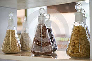 Various raw cereals, grains, beans and pasta for cooking healthy food in glass jars on a wooden shelf.