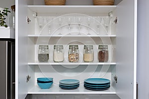 Various seeds in storage jars in pantry, white modern kitchen in background. Smart kitchen organization