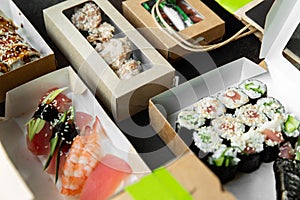 Various selection of sushi, rolls and gunkans in craft boxes on a dark background. Food at home. Delivery concept