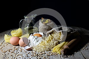 Various Shapes and Colors of Pasta and Ingredients for Pasta on Rustic Wooden Table, Black Background