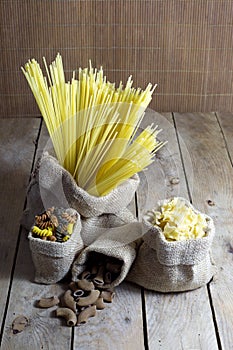 Various Shapes of Pasta In Jute Bags on Wooden Table