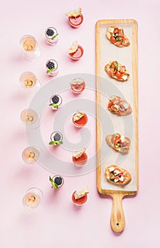 Various snacks, brushetta sandwiches, gazpacho shots, desserts over pink background