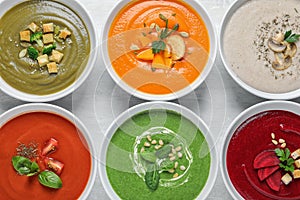 Various soups in bowls on wooden background, top view.