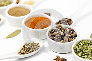 Various spices for cooking, laid out in white bowls and spoons, close-up.