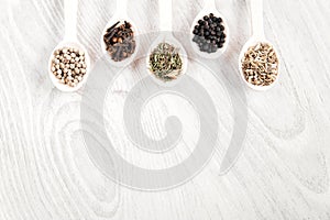 Various spices and herbs in wooden spoons on white table background. Black and white pepper, cl