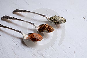 Various spices in spoons on white wood table background.n