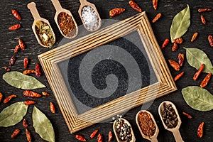 Various spices in wooden spoons on dark stone table