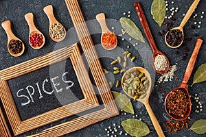 Various spices in wooden spoons on dark stone table.