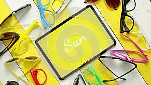 Various style, shape and colour sunglasses. Tablet in the middle with text SUN.