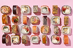 Various sushi rolls on pink background, top view