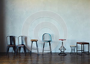 Various types of chairs and stools stand against the gray wall.