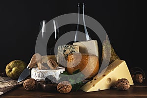 Various types of cheese with glass of wine on rustic wooden table. Dark background