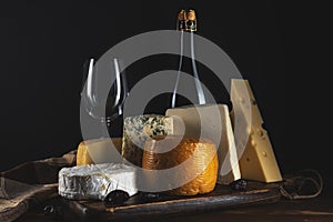 Various types of cheese with glass of wine on rustic wooden table. Dark background