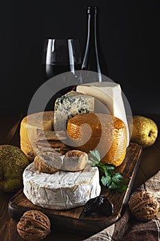 Various types of cheese with glass of wine on rustic wooden table. Dark background