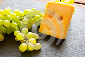 Various types of cheese with green grapes on black slate cheeseboard on table