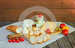 Various types of cheese, tomatoes and baguette on rustic wooden table