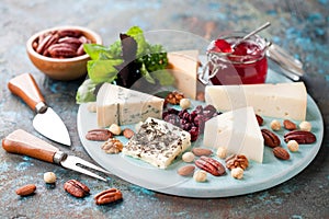 Various types of cheese on a wooden plate with jam, nuts and dried cranberries