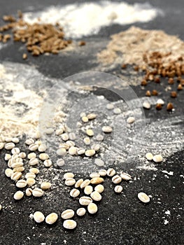 Various types of flour on a black textured stone surface. Buckwheat, wheat and barley flour