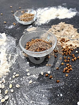 Various types of flour on a black textured stone surface. Buckwheat, wheat and barley flour