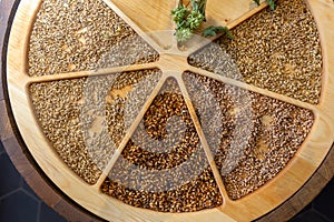 Various types of malting malt and a dried branch of hops on a wooden tray