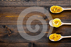 Various types of pasta concept. Fusilli, penne, fettuccine in spoons on dark wooden background top view copy space