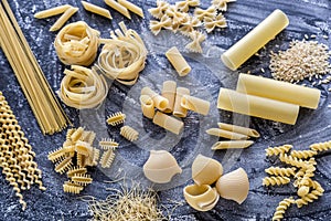 Various types of pasta on the dark flour dusted background