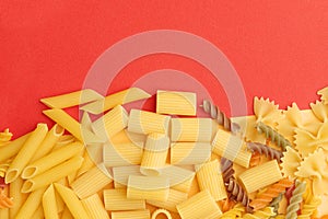 Various types of uncooked pasta on a orange background top view. Place for text.