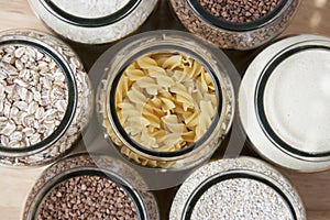 Various uncooked cereals, grains, and pasta for healthy cooking in glass jars on wooden table. Top view. Clean eating, balanced di
