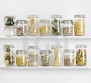 Various uncooked groceries in glass jars arranged on wooden shelves