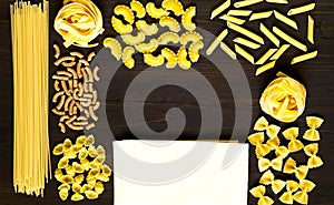 Various uncooked pasta on dark wooden background. Food concept. Flat lay. Top view, copy space