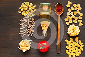 Various uncooked pasta and wooden spoon with spices on dark background. Food concept. Flat lay. Top view, copy space.