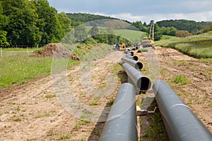 Various unplugged gas pipes lead in an idyllic landscape to the background with equippment to pipe laying